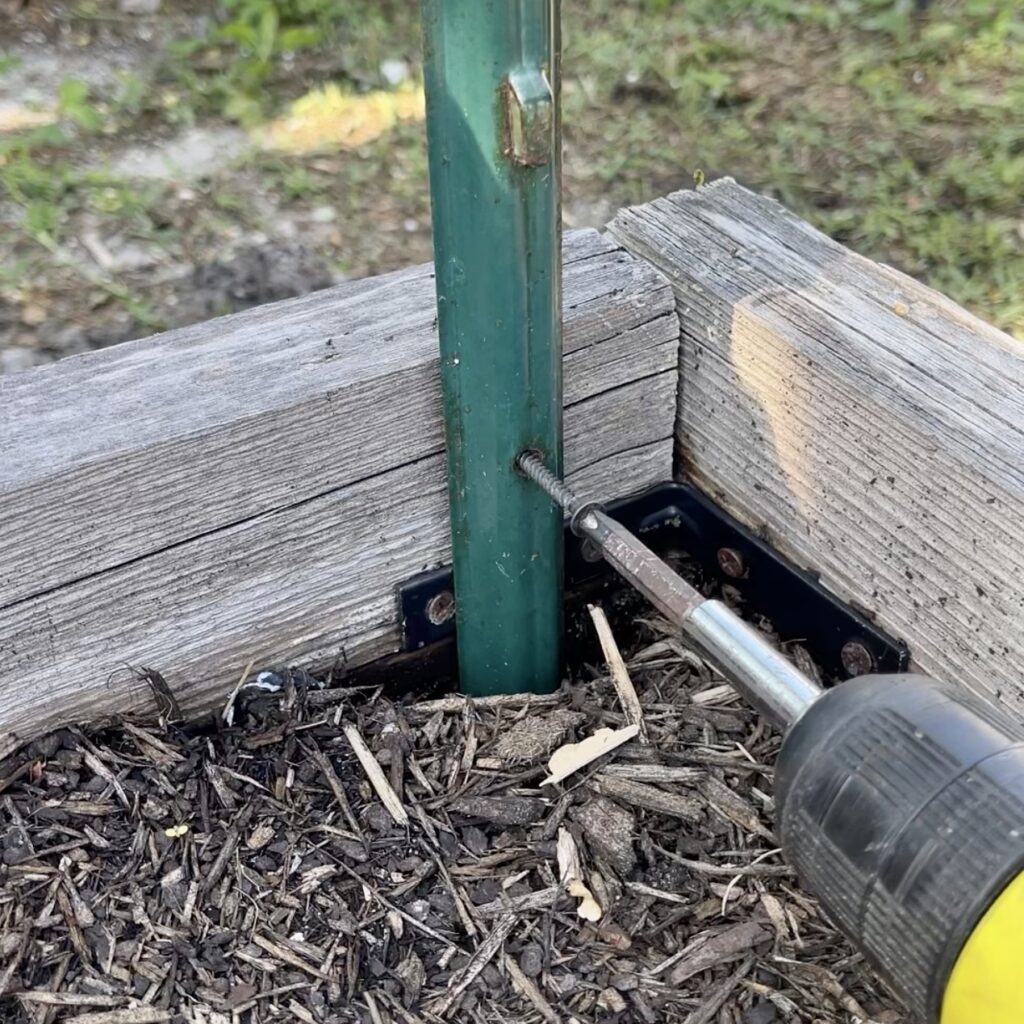 drill connecting metal stake to wood in garden bed