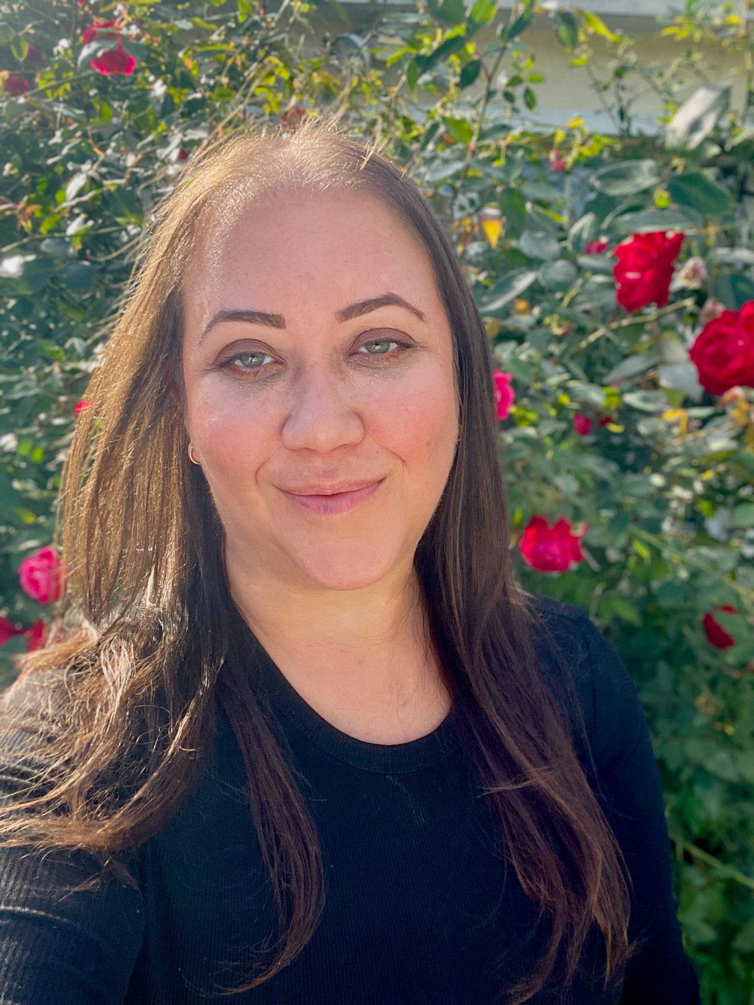 Head shot of a woman with long brown hair standing in front of a large bush with red flowers