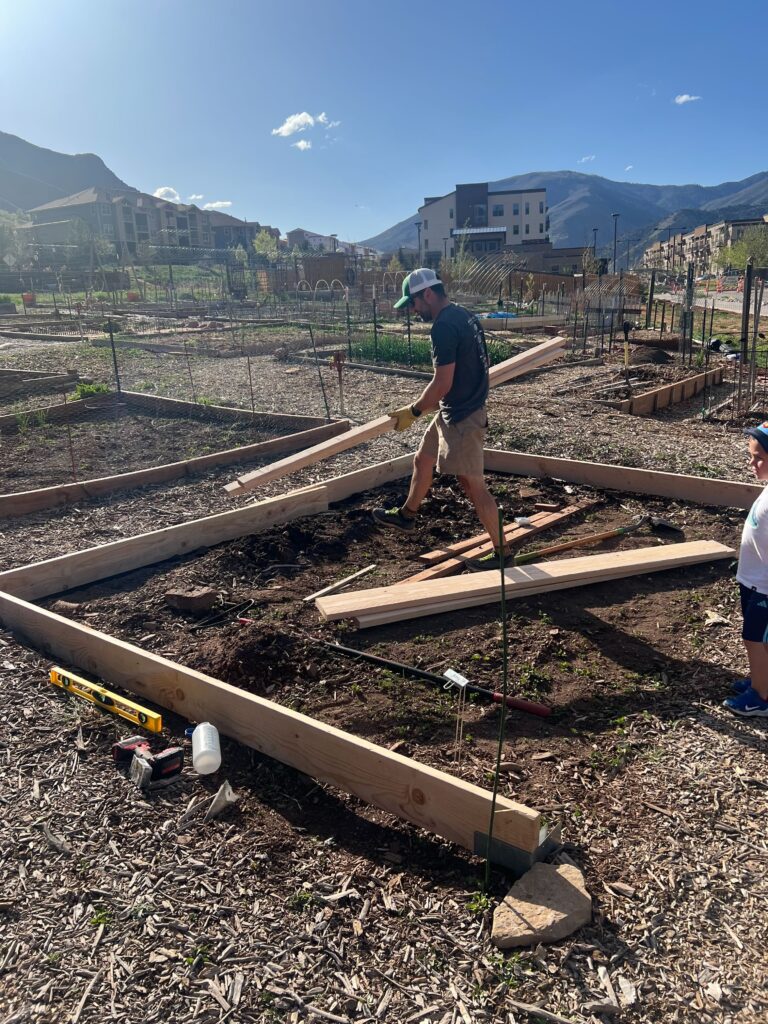 A man holding a piece of lumber building the sides to a garden plot