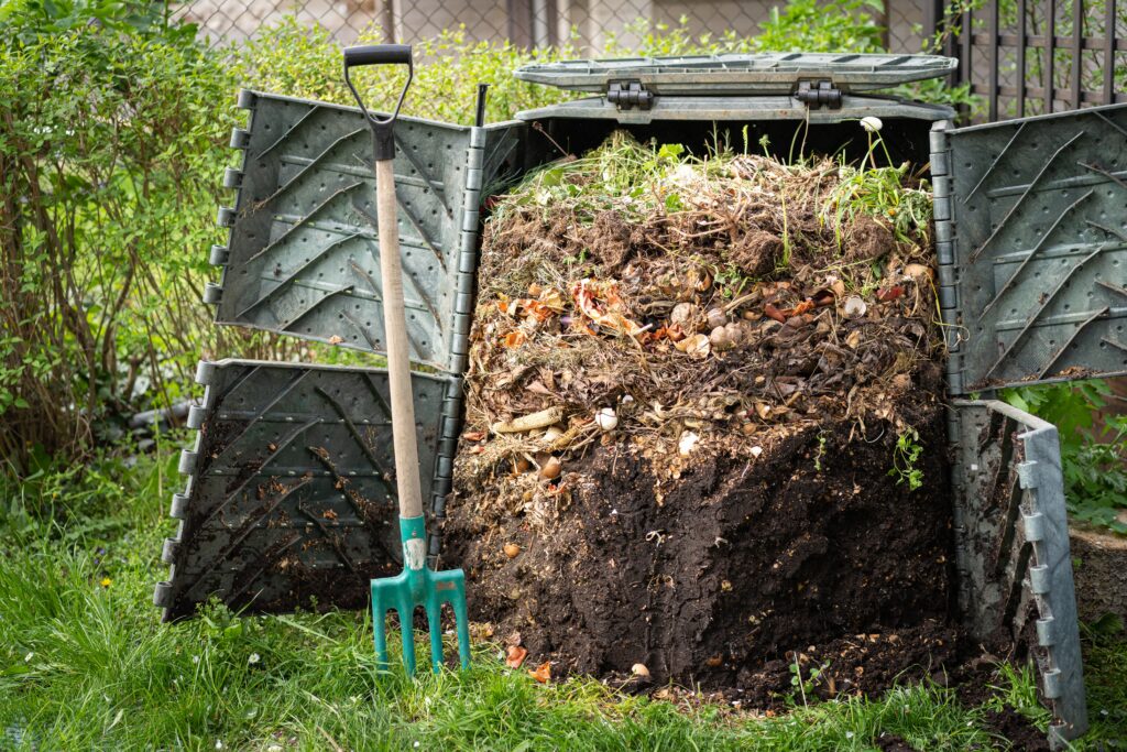 A large compost bin with the doors open to reveal healthy soil and a pitch fork leaning again the open door