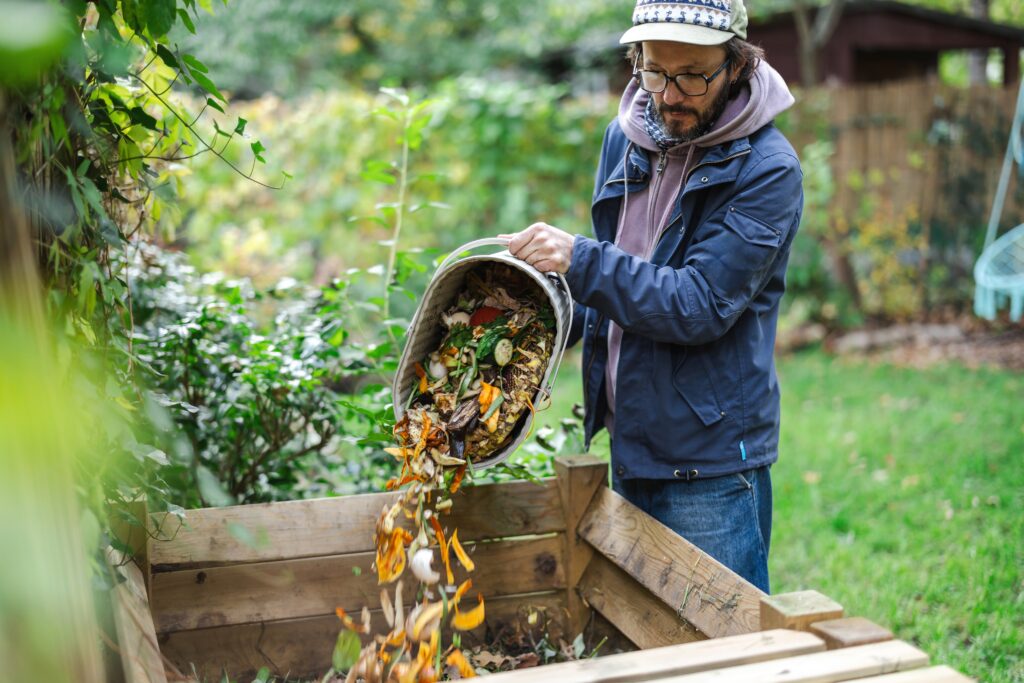 Man dumping a pale of leaves and food scraps into a wooden compost bin