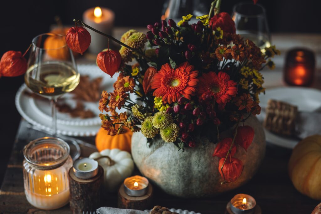 fall arrangement with red, purple and green florals and foliage on a set table with pumpkins and candles