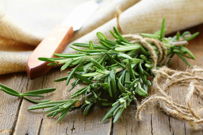 a bundle of cut rosemary tied together with twine and laying on a wooden surface